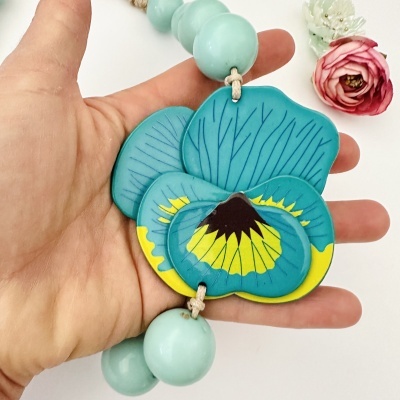 Colar de contas azuis com pendente floral azul e amarelo na mão