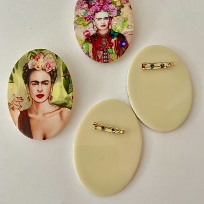 Broches ovais com imagens de Frida Kahlo e fechos dourados na parte traseira
