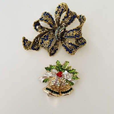 Dois broches decorativos, um laço dourado com azul e um sino dourado com verde e vermelho