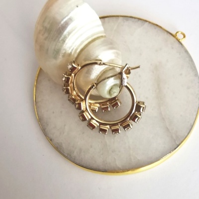 Brincos dourados sobre base de mármore branco com concha