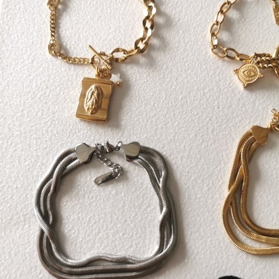 Quatro pulseiras, duas douradas com pendentes e duas em prata e dourado com texturas diversas