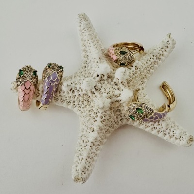 Conjunto de joias com anel e brincos com detalhes de escamas em esmalte rosa e violeta e pedras verdes sobre estrela-do-mar.