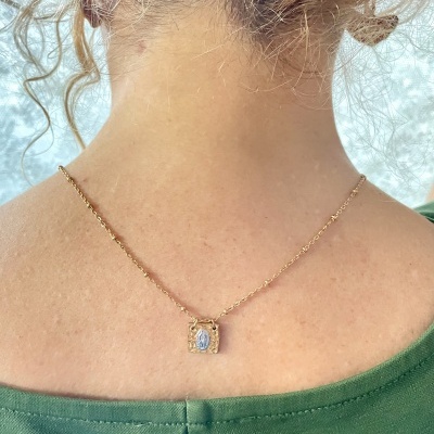 Colar dourado com pendente de Nossa Senhora azul e branco no pescoço