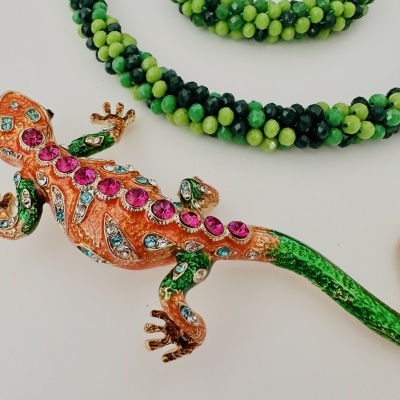 Colar e pulseira de contas verdes com broche lagarto colorido em fundo branco