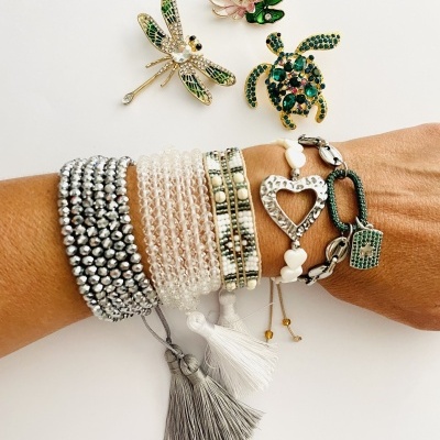 Pulseiras de diferentes estilos e cores com três broches em fundo branco.