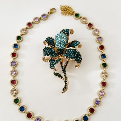 Colar dourado com pedras coloridas em torno de broche flor azul