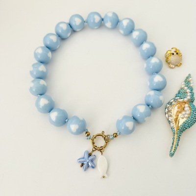 Pulseira azul com corações brancos e pendentes marinhos sobre fundo branco