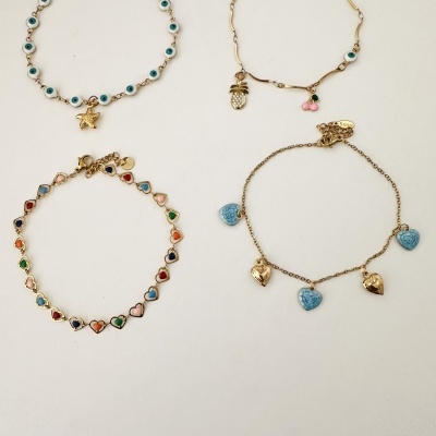 Quatro pulseiras douradas com diferentes pendentes e detalhes coloridos colocadas sobre fundo branco.