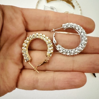 Brincos argola dourado e prateado com pedras brilhantes na mão