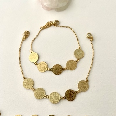 Três pulseiras douradas com medalhas redondas e uma pedra rosa translúcida