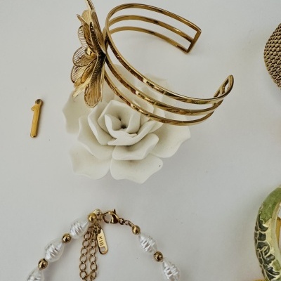 Bracelete dourado e pulseira com pérolas e esferas douradas em fundo branco.
