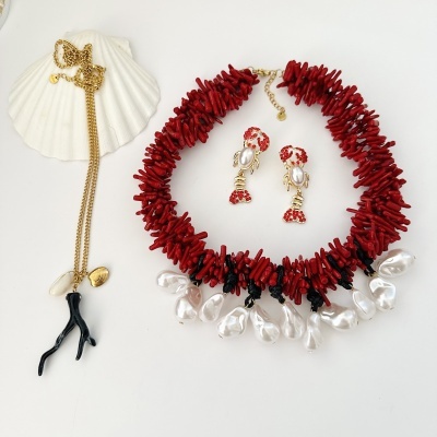 Conjunto de joalharia com colar vermelho e pérolas, brincos de lagosta dourada com pedras vermelhas e pérola, e colar dourado com pendente preto e concha.
