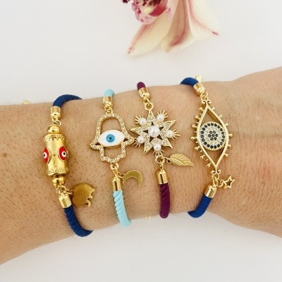 Pulseiras coloridas com detalhes dourados e pedras azuis num braço com fundo branco e flor rosa