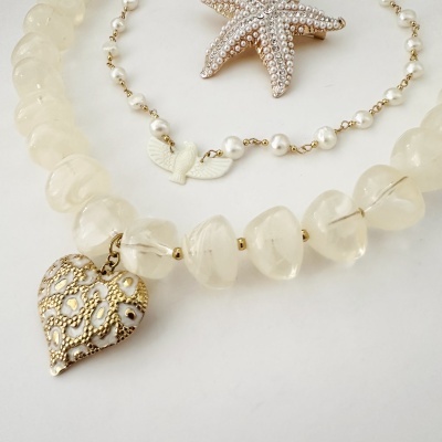 Jóias em branco, dourado, pérolas e cristal sobre fundo branco.