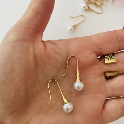 Brincos dourados com pérolas na mão sobre fundo branco