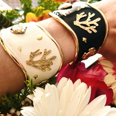 Pulseiras esmalte branco e preto com detalhes dourados em pulso cercado por flores