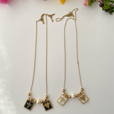 Dois colares dourados com pendentes quadrados bordados e contas, sobre fundo branco com flores coloridas.