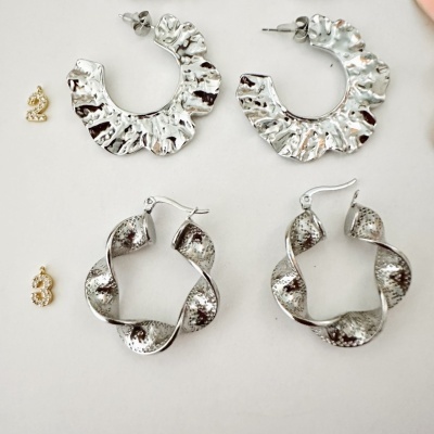 Dois pares de brincos prateados com texturas distintas sobre fundo branco