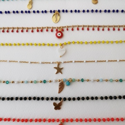 Colares ou pulseiras coloridas com pingentes variados em correntes douradas sobre fundo branco.