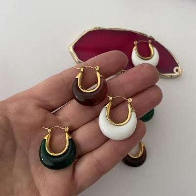 Brincos argola com detalhes dourados em acrílico verde, castanho e branco sobre mão feminina e mesa branca