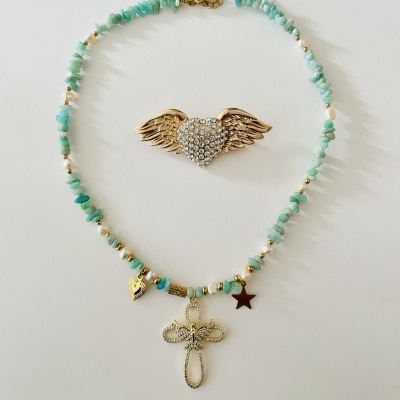 Colar azul-esverdeado com cruz e broche dourado em forma de coração com asas