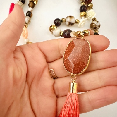 Colar com contas variadas, pedra oval dourada e franja vermelha na mão
