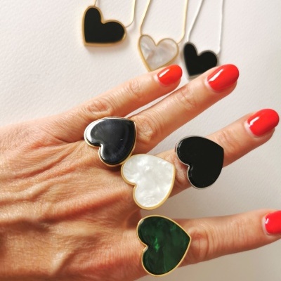 Anéis e colares com pendentes de coração coloridos em mão com unhas vermelhas