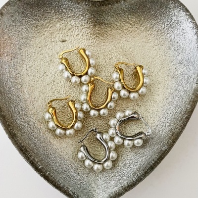 Brincos dourados e prateados com pérolas numa travessa prateada em forma de coração.