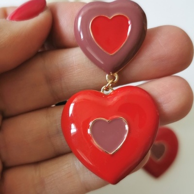 Brinco de dois corações, vermelho e castanho avermelhado, segurado pela mão