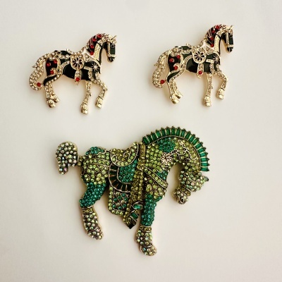 Três broches de cavalos com pedras coloridas sobre fundo branco.