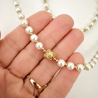 Colar de pérolas e contas douradas numa mão.