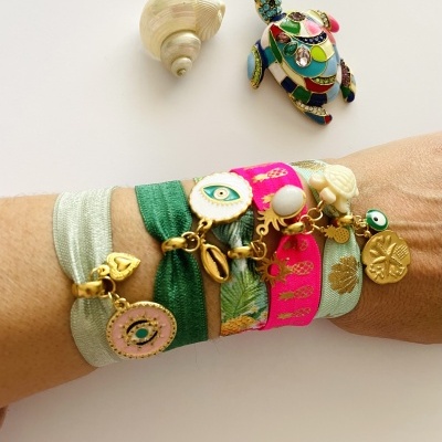 Pulseiras multicoloridas com pendentes dourados e concha sobre pulso feminino.