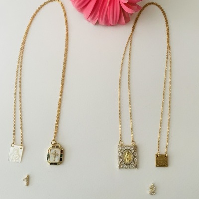 Duas correntes douradas com medalhões religiosos em fundo branco, botão rosa acima