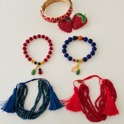 Conjunto de bijuteria com pulseira dourada, brincos de morango, pulseiras de contas e colares com franjas em azul e vermelho