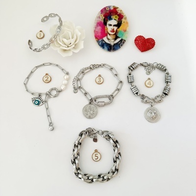 Cinco pulseiras prateadas com diferentes pendentes e uma decoração ao redor, em fundo branco
