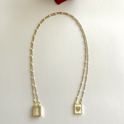 Colar dourado com pendentes retangulares e uma rosa vermelha ao fundo