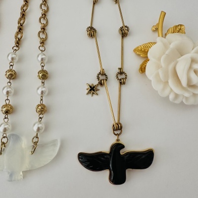 Colares dourados com pingentes de pássaros e flor branca com detalhes dourados