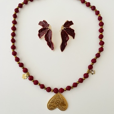 Conjunto de colar com pendente em forma de coração dourado e brincos vermelhos escuros sobre fundo branco