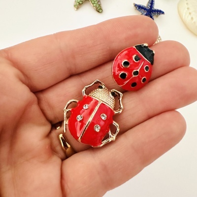 Broches de joaninhas vermelhas e douradas com manchas pretas e brilhantes na mão sobre fundo branco