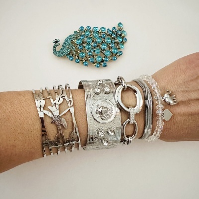 Pulseiras metálicas e de contas transparentes no pulso com uma joia azul em forma de pavão no fundo branco