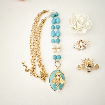 Colar com contas azuis, corrente dourada, pendente oval com abelha dourada com pérola, dois broches de abelhas douradas com pérolas, flor branca