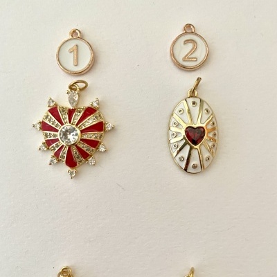 Dois pendentes em metal dourado com esmalte vermelho e branco, com etiquetas numeradas 1 e 2 sobre fundo branco.