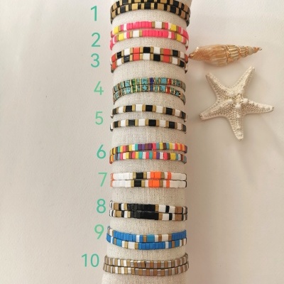 Pulseiras multicoloridas de contas pequenas em almofada clara com concha e estrela do mar ao lado