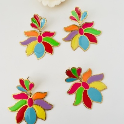 Brincos coloridos em forma de flor sobre fundo branco com flor decorativa branca