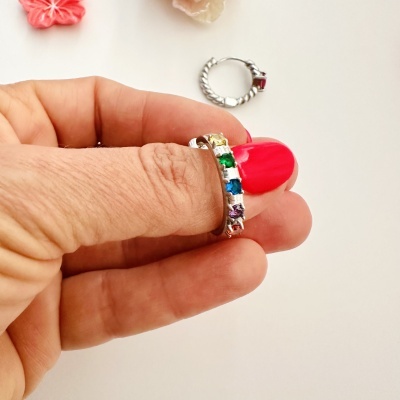 Anel prateado com pedras coloridas numa mão com unhas vermelhas