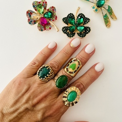 Mão com anéis e três broches coloridos em fundo branco