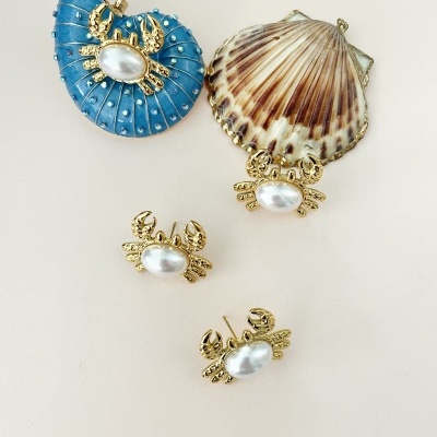 Conjunto de joias com caranguejo dourado e perola branco sobre conchas e fundo branco