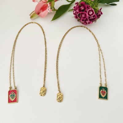 Três colares dourados com pendentes variados e flores cor-de-rosa sobre fundo branco.