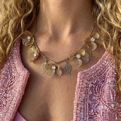 Colar dourado com flores e folhas usado com casaco rosa bordado com lantejoulas