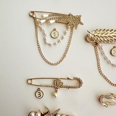 Alfinetes dourados com pérolas, strass e números 1, 2 e 3 em fundo branco